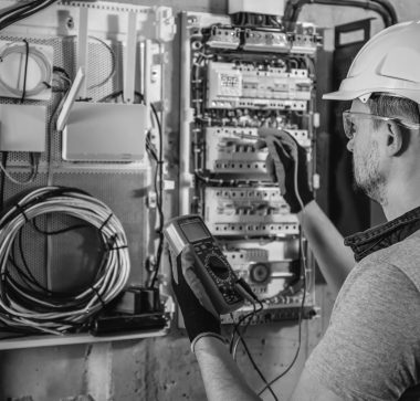 Man, an electrical technician working in a switchboard with fuses. Installation and connection of electrical equipment. Professional uses a tablet.