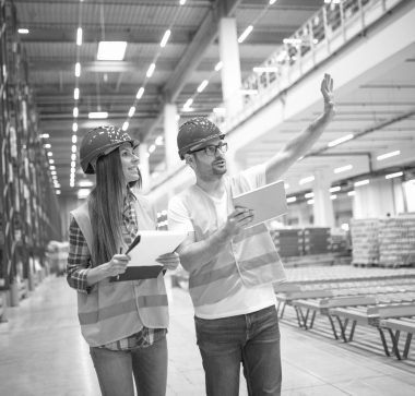 Warehouse workers consulting each other in large factory storage area. Male employee sharing his idea to his coworker about increasing productivity of distribution to the market.